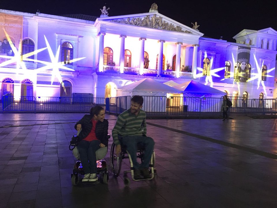 Two wheelchair users at night in front of the Teatro Sucre in Quito